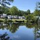 Campground with RVs parked along a calm pond, trees reflect in water on a sunny day.
