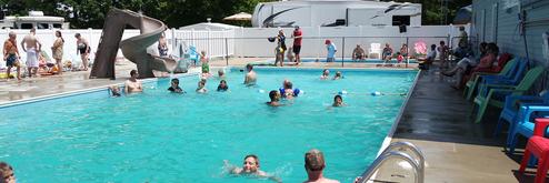 Photograph of the campground's outdoor swimming pool with campers and nearby RVs visible; image is from the site's header (2019 pool image) indicating it's a facility at this property.
