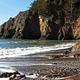 The beach at Kirby Cove, with dramatic cliffs, dark volcanic sand, and frothy water. 