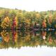 Reflective lakeshore with vivid fall foliage and a swim platform visible at left — another clear view of the beachfront and natural beauty on the property.