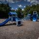 Playground equipment on gravel with trees in background — shows the campground’s play area/amenities (gallery image on main site).
