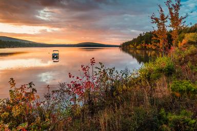 Scenic lakeside sunrise/sunset with a boat on calm water — represents the campground’s lake setting and atmosphere for guests (supports waterfront character shown on the property page).