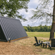 Small A-frame glamping unit next to trees and open field with Adirondack chairs — useful view of glamping site layout and surrounding scenery from the property images.