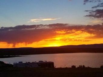 Dramatic sunset with an RV silhouette along the lakefront — clearly depicts an on-site RV and lakeside setting referenced on the RV Park page, useful for showing available RV pitches and scenery (source: /rv-park).