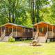 Row of wooden cabins with picnic tables on grassy, shaded lots — directly matches the site’s accommodations imagery on the Amenities/Accommodations pages.