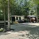 Shows an RV parked in a wooded, gravel campsite with site amenities (picnic area, shelter) — useful depiction of RV accommodations from the site gallery/home content.