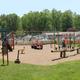 Clear daytime wide shot of onsite playground and surrounding open lawn, showing play equipment and campground buildings — good for facility/grounds overview (page slider image).