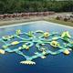 Aerial/oblique shot showing lake inflatables with a row of cabins or park-models along the shore — highlights lodging/rental units and water feature on the property (campgrounds-main_0069).