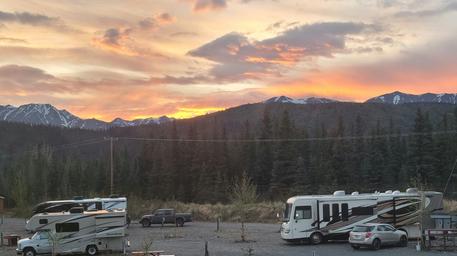 Sunset overview showing multiple RVs parked on gravel pads with mountain backdrop — clear overall view of the RV parking area and surrounding scenery, matching the park layout on the site.
