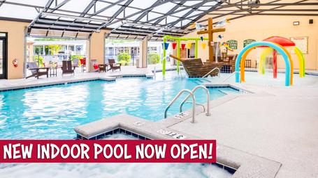 Indoor swimming pool with a pirate ship water feature, rainbow water slides, and lounge chairs, with a bold banner at the bottom reading "New Indoor Pool Now Open!"