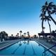 Wide pool view at sunset with palm trees, pool deck seating and the resort buildings visible — attractive pool/facilities photo that highlights ambiance (from the homepage).