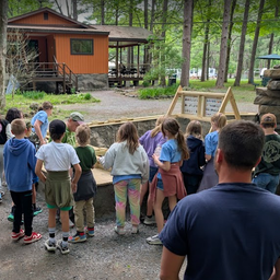 Exterior view of campground grounds with a cabin/pavilion and children gathered at an activity — shows on-site facilities and family programming (from the Birthdays page).