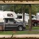 Shows multiple RVs/truck campers parked on level, wooded RV sites with picnic tables and fire rings — useful view of typical RV pitches. Comes from the homepage gallery slider for the property.