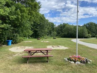 Open grassy recreation area with picnic table, horseshoe/sand pits, flagpole and campground road — useful to show on-site outdoor amenities (from Amenities page).