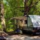 Clear photo of an RV parked at a wooded campsite with picnic table and mat — useful for showing RV/campsite accommodations; appears on the campground page.