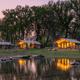 Twilight lakeside shot of illuminated glamping cabin/tent reflecting in the pond — strong scenic image showcasing waterfront accommodations and ambiance (used on homepage).