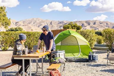 Tent campsite on a gravel pad with picnic table, shade plantings and desert mountain backdrop — good view of tent camping areas and surrounding scenery on the KOA grounds (from the campground waystostay photos).