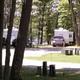 Panoramic strip showing multiple RVs and wooded campsites — useful depiction of wooded campground sites and spacing. Shown on the Accommodations page as a campground scene.
