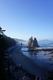 Rocky sea stacks rise from the sandy, ocean shore just south of Hole-in-the-Wall. Driftwood lays scattered on the beach.