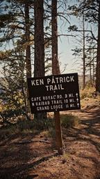 Ken Patrick Trail sign in a pine forest, listing Cape Royal and Grizzly Ridge trail distances.