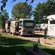 Two RVs parked at a sunny campground with picnic tables.