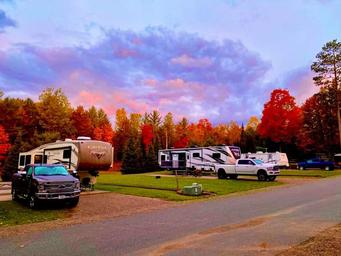 Row of RVs parked at designated concrete pads with hookups and road — good overview of RV pitches and site layout. Image appears on the Home page (fall-pic) showing campground RV sites.