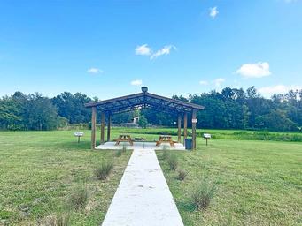 Covered picnic pavilion set in open lawn with a pond/landscape beyond — shows scenic grounds and a park amenity consistent with the property description.