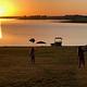 Two children stand near the shore of a lake at sunset