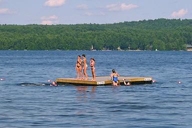 Floating swim platform with people — highlights water activities and swim area available at the campground's lakefront.
