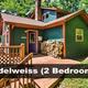 Bright, well-composed exterior of 'Edelweiss' 2-bedroom cabin with deck and stacked firewood — useful cabin photo from the property listings on the homepage.