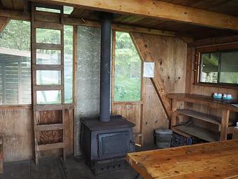 Interior of wood cabin with shelves, tables, stove and ladder to loft