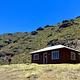 backpacker walks up to cabin at the base of a hill