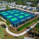 Aerial/angled photo focused on the multi-court (pickleball/tennis) facility with surrounding landscaping and nearby cottages — from the site gallery highlighting amenities.
