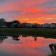 A blazing orange sunset reflected in the park pond, with RVs lined up along the bank