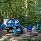 Tent and 4 camp chairs on wood chip campsite.  Site has a picnic table, fire ring/grill and lantern post.