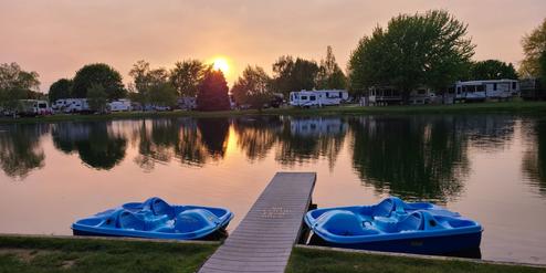 Evening view across the central pond with dock and paddleboats, RVs and cabins visible around the shoreline — highlights the park’s pond recreation area referenced on the homepage.