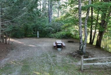 Individual tent/campsite area with picnic table, fire ring and tree buffer adjacent to water — useful detail photo showing a typical tent/campsite setup on the grounds.