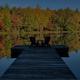 Wide scenic view of a dock on a calm lake framed by trees — good property overview showing on-site waterfront (used as hero/background image on the campground homepage).