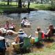 Shows people relaxing in the shallow creek that runs through the property — highlights a distinctive on-site water recreation feature (slider5 image).