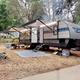 Large travel trailer at a developed campsite with mat, picnic and road — useful close view of an RV setup and site amenities on the property.