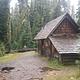 Fire ring in front of log cabin with attached, covered wood shed  in misty conifer forest.