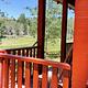 bright red wooden rails frame the front porch of the guard station where a wooden chair offers a view of the adjacent meadow on a sunny day.