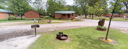 Row of cabins with grills, picnic table and paved campground road — useful for showing rental cabins and campsite layout; appears in the site's campground visuals.