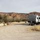 Campsite with trailer parking in parking area. Red rock cliffs line the horizon in the background.