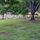 A grassy field with a few trees. A pavilion is in the background.