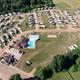 High-resolution aerial/drone overview showing RV pads, roads, central clubhouse/pool, and surrounding green space — matches site’s drone/home-slider imagery and provides clear property layout.