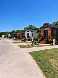 Row of onsite tiny homes/cabins with paved pads, picnic tables and utility pedestals — clear, high-quality photo from the property’s gallery highlighting cabin accommodations.