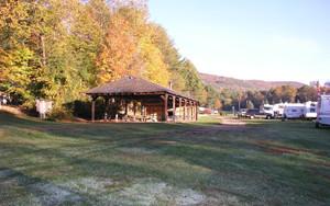 Pavilion pictured on a mown field with nearby RV sites and trees — good overall view of a central facility/amenity on the campground.