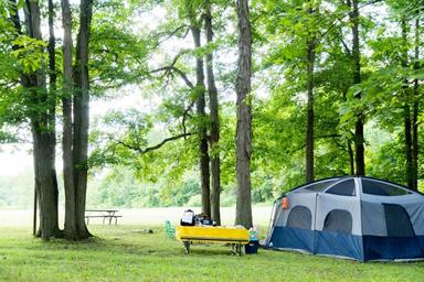 Tent and picnic setup under trees — showcases a typical tent campsite in a wooded area, useful for campers. Image is used on the Weekend Camping page of the site.