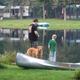 People fishing at the lake with a canoe and reflected cabins in background — shows waterfront activity and nearby cabin sites (homepage slider).